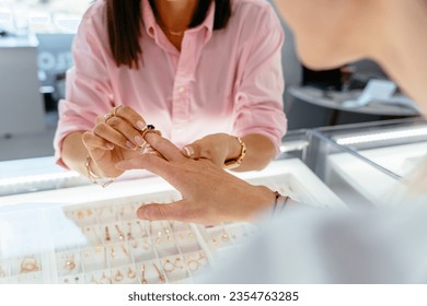 Sale, consumerism, shopping and people concept. Unrecognizable woman client choosing and trying ring at jewelry store. Saleswoman suggesting gold rings to female customer. - Powered by Shutterstock