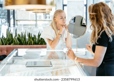 Sale, consumerism, shopping and people concept. Attractive blond woman choosing and trying ring and earrings at jewelry store. - Powered by Shutterstock