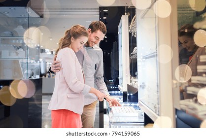 Sale, Consumerism, Shopping And People Concept - Happy Couple Choosing Engagement Ring At Jewelry Store In Mall