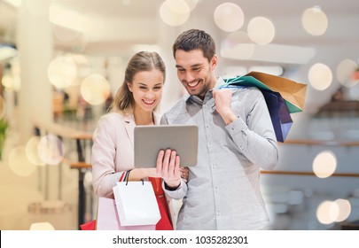 Sale, Consumerism, Technology And People Concept - Happy Young Couple With Shopping Bags And Tablet Pc Computer Pointing Finger In Mall