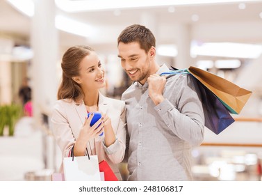 sale, consumerism, technology and people concept - happy young couple with shopping bags and smartphone talking in mall - Powered by Shutterstock