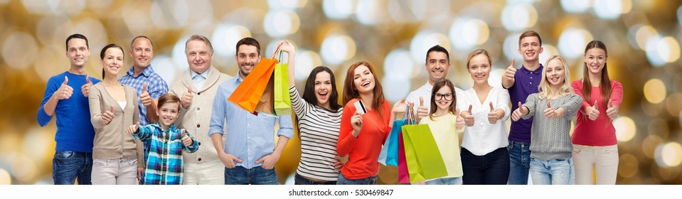 Sale, Family, Generation And People Concept - Group Of Happy Men And Women With Shopping Bags And Credit Card Showing Thumbs Up Over Holidays Lights Background