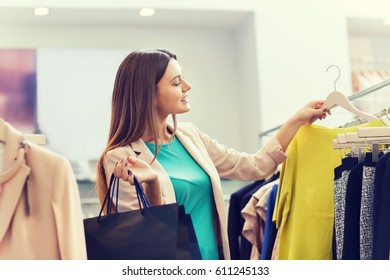 Sale, Fashion, Consumerism And People Concept - Happy Young Woman With Shopping Bags Choosing Clothes In Mall Or Clothing Store