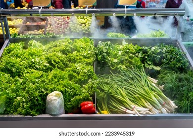 Sale of fresh green vegetables - lettuce salad, parsley, dill, green onions, herbs. Fresh herbs on display at grocery store under cooling water steam. Vegetables sprayed with mist water from nozzles - Shutterstock ID 2233945319