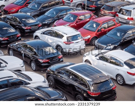 Sale of new and used cars in a dealership. Lots of cars in the car park. Black, white, silver and red cars of unknown brands