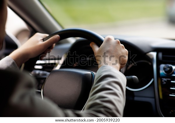 Sale and rental transport. Driver holding steering\
wheel sitting in new auto, enjoy road trip to work. Young\
businessman drives modern new car on road, view in cabin, cropped,\
close up, free space