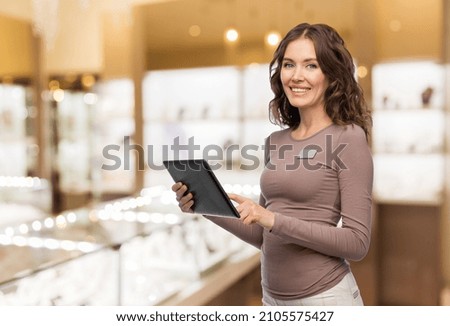 sale, shopping and business concept - happy female shop assistant with tablet pc computer name tag over jewelry store background
