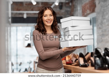 sale, shopping and business concept - happy female shop assistant or saleswoman holding three shoe boxes over store background