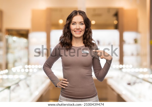 sale, shopping\
and business concept - happy female shop assistant showing her name\
tag over jewelry store\
background