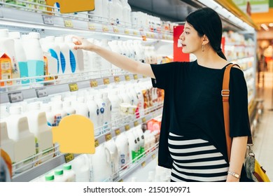 Sale Shopping Consumerism Pregnancy And People Concept. Happy Young Asian Chinese Pregnant Woman Holding Milk Bottle In Market. Future Mom With Big Belly Take Down From Shelves In Hypermarket Indoors