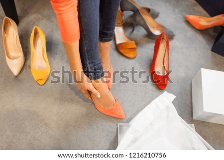 sale, shopping, fashion and people concept - young woman choosing high heeled shoes at store