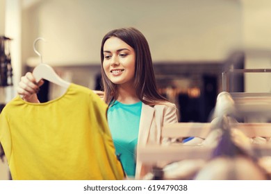 Sale, Shopping, Fashion, Style And People Concept - Happy Young Woman Choosing Clothes In Mall Or Clothing Store