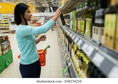 Sale, Shopping, Food, Consumerism And People Concept - Woman With Basket Buying Olive Oil At Grocery Store Or Supermarket