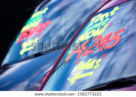 For sale sign price painted on car windshield at automobile dealership  lot, discount car sales, special deals, slashing prices, competitive pricing, low automobile sales, 