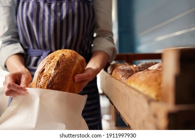 Sales Assistant In Bakery Putting Freshly Baked Organic Sourdough Bread Loaf Into Sustainable Paper Bag