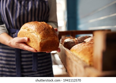 Sales Assistant In Bakery Putting Freshly Baked Organic Sourdough Bread Loaf Into Wooden Tray - Powered by Shutterstock