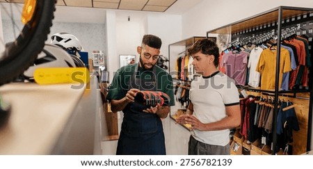 Sales assistant explaining features of a cycling shoe to a male customer, offering expert advice in a modern sports retail store filled with activewear and equipment