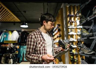 Sales assistant sports travel store makes inventory hiking boots. Travel goods store theme. Clothes and footwear for sports and travel. Store manager near shelves with hiking boots makes check list. - Powered by Shutterstock