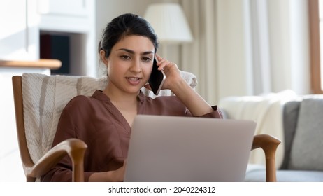 Sales By Telephone. Busy Young Ethnic Female Telemarketer Talk To Client By Mobile Phone Fill In Order Form On Laptop Online. Indian Woman Remote Specialist Use Computer And Cellphone At Distant Job