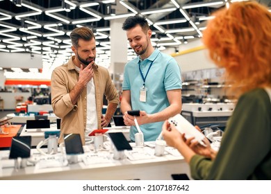 Sales consultant advises man who chooses new smartphone in store of household appliances, electronics and gadgets. Professional consultation in store. Sale Day. - Shutterstock ID 2107187642