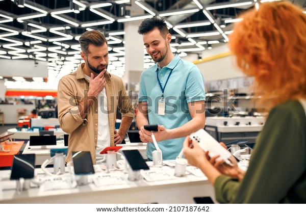 Sales consultant advises\
man who chooses new smartphone in store of household appliances,\
electronics and gadgets. Professional consultation in store. Sale\
Day.