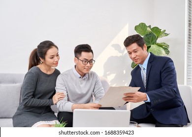 Sales Consultant Showing New Investment Plans To Young Asian Couple