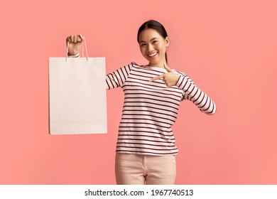 Sales And Consumerism Concept. Happy Asian Woman Holding And Pointing At Blank Paper Shopping Bag, Cheerful Young Korean Shopaholic Female Demonstrating Copy Space For Your Advertisement, Mockup