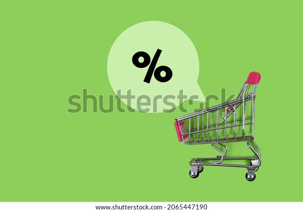 Sales and discounts concept, shopping\
cart and the percent icon above it on green\
background
