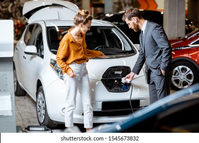 Sales Manager Showing How To Charge Electric Car To A Young Client, Plugging Wire Into The Car Socket At The Car Dealership