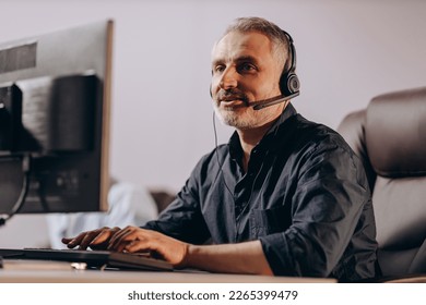 Sales manager talking to client via headset. Middle-aged hotline operator typing on computer keyboard. Customer support agent in office - Powered by Shutterstock