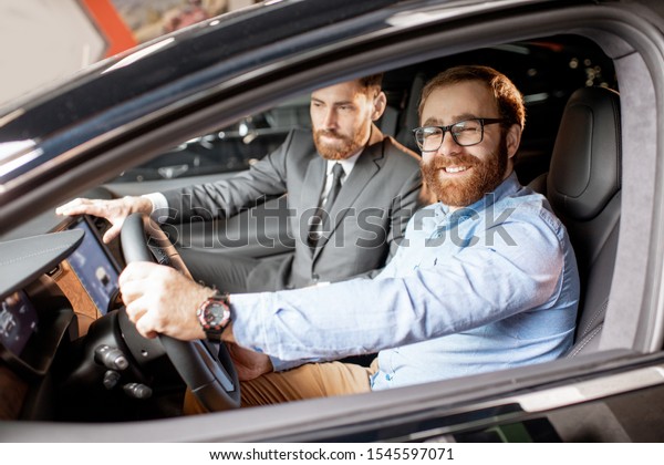 Sales\
manager with a young client inspecting vehicle interior at the car\
dealership. Man choosing new electric car to\
buy