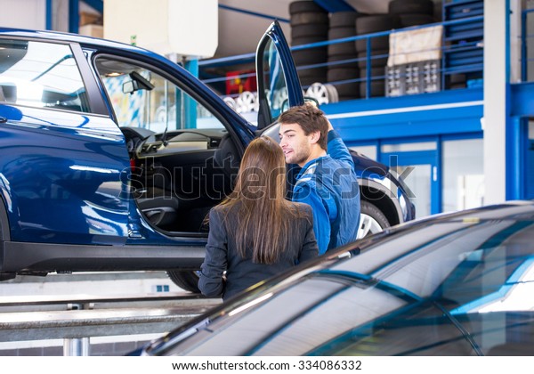 A sales mechanic shows the vehicle he\
has been working on to a business woman, who is interested in\
buying it at a used car dealership\
garage