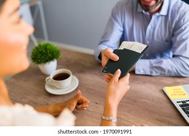 Sales Representative Giving A Passport And Plane Tickets To A Female Customer Sitting At His Desk At The Travel Agency