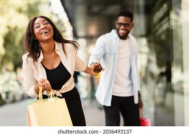 Sales Season. Portrait Of Smiling Excited African American Lady Pulling Boyfriend To Shopping Store To Buy New Clothes, Fooling And Running To Mall Together. Discount, Fun, Purchase And Retail
