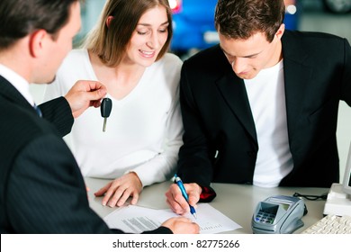 Sales situation in a car dealership, the young couple is signing the sales contract and gets the key for the new car