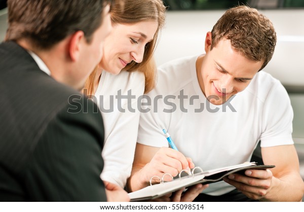 Sales
situation in a car dealership, the young couple is signing the
sales contract to get the new car in the
background