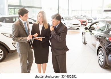 Sales Team Look At A Clipboard At New Car Showroom