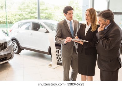 Sales Team Look At A Clipboard At New Car Showroom