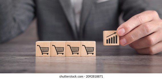 Sales Volume Increase. Male Hand Showing Shopping Carts And Growth Chart On Wooden Cubes