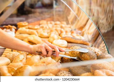 Sales woman in baker shop putting bread roll in paper bag for a customer - Powered by Shutterstock