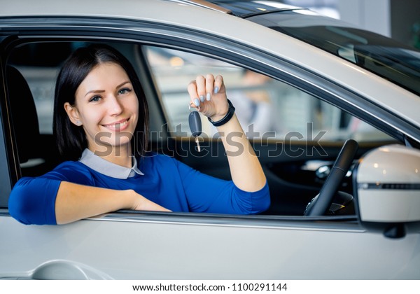 Sales\
woman sitting in a car showing car keys at\
showroom