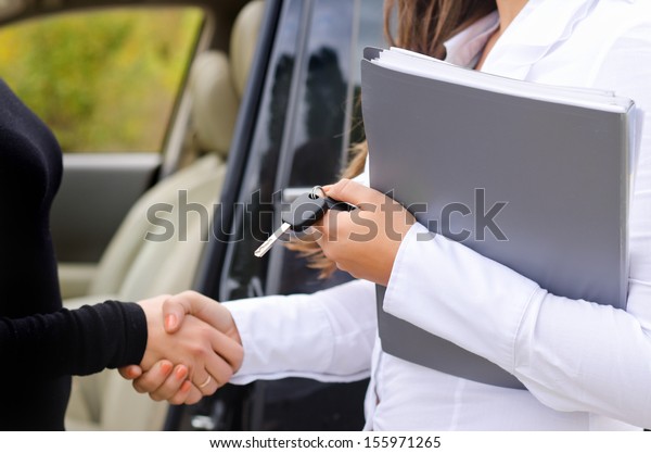 Saleslady selling a car to a new female owner and\
shaking hands to close the deal and congratulate her client while\
holding the paperwork and\
keys