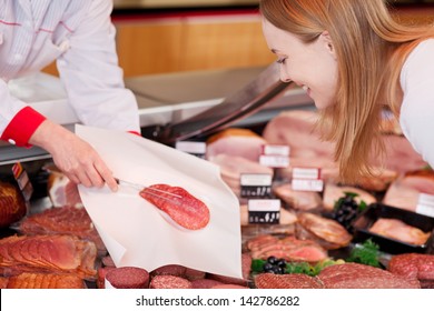 Saleslady serving sliced salami on a sheet of tissue paper with a fork for a discerning female shopper - Powered by Shutterstock