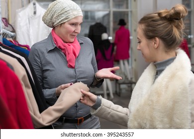 Saleslady In Uniform Showing Variety Of Winter And Spring Jackets To Young Female Customer In Retail Store Explaining Features And Trying To Get A Deal