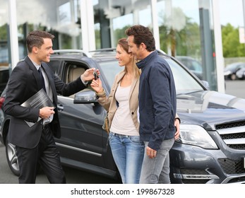 Salesman in car dealership giving keys to clients