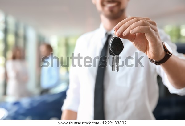 Salesman with\
car keys in auto dealership,\
closeup