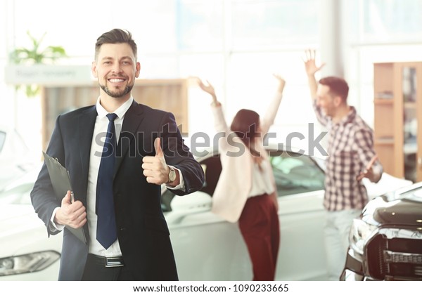 Salesman with clipboard and happy couple in salon.\
Buying new car