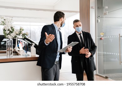 Salesman And Customer In A Car Dealership Wearing Masks During Pandemic, Holding Catalogue