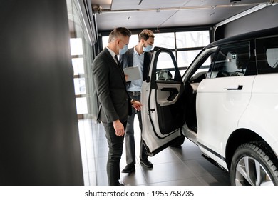 Salesman And Customer In A Car Dealership Wearing Masks During Pandemic, Looking Indide A Car