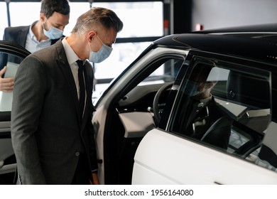 Salesman And Customer In A Car Dealership Wearing Masks During Pandemic, Looking Indide A Car